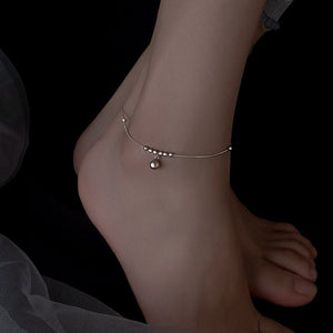 Silver anklet on a foot against a dark background