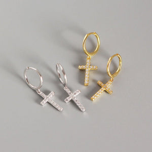 Three pairs of cross-shaped earrings in gold, silver, and gold on a gray background.