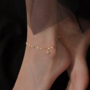 Gold anklet on a person's ankle against a dark background