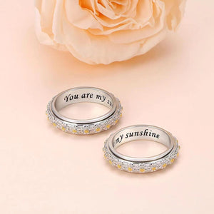 Two silver rings with 'You are my sunshine' engraving on a soft peach background with a rose.