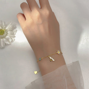 A sterling silver stacking bracelet with daisy flower charms and a small bell, displayed on a blue background with white flowers.