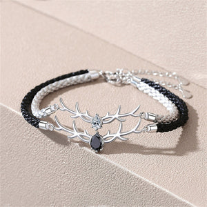 Bracelet with silver antler design and black and white cord on a beige background