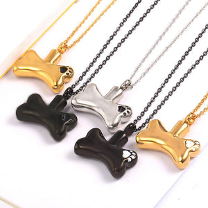 Dog bone-shaped pendants in gold, black, and silver on chains against a white background.