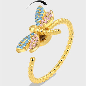 Gold butterfly ring with blue and pink gemstones on a light gray background