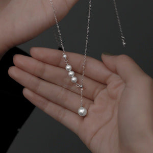 Hand holding a pearl necklace with silver chain on a gray background