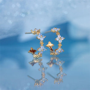 Gold and opal hoop earrings on a reflective blue surface with a blurred background