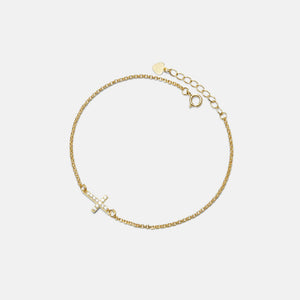 Gold bracelet with a small cross charm on a light gray background