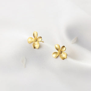 Gold flower-shaped earrings on a white fabric background