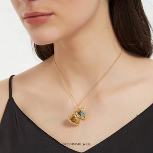 Gold heart locket necklace shown open, worn on a delicate chain on a model’s neck.