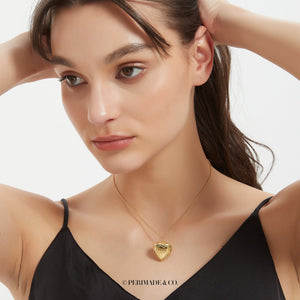Gold heart locket necklace with vintage engraved design, worn on a delicate chain on a model’s neck.