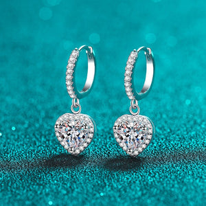 Heart-shaped silver earrings with clear gemstones on a teal background
