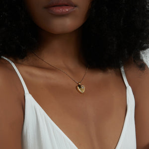 Gold heart locket necklace with a paw design, worn on a delicate chain on a model’s neck.