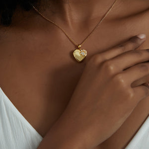 Gold heart locket necklace with a paw design, worn on a delicate chain on a model’s neck.