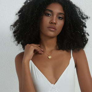 Gold heart locket necklace with a paw design, worn on a delicate chain on a model’s neck.