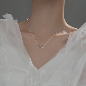 A person wearing a white v-neck shirt showcasing a sterling silver necklace with a small crane charm, with a subtle chain link.