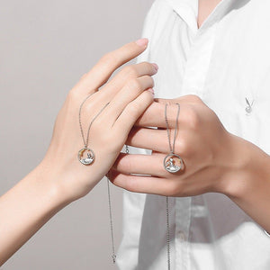 Two hands each holding a silver necklace with the little prince and fox pendant on a light background