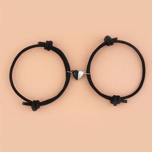 Two black hair ties with a heart-shaped metal clip on a beige background