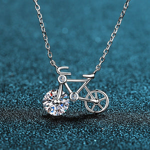 Silver bicycle-shaped necklace with a clear gemstone on a blue textured background