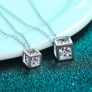 Silver cube-shaped pendants with clear gemstones on a blue textured surface.