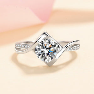 Silver ring with a large diamond and smaller diamonds on the band against a soft pink background