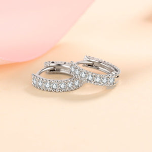 Pair of silver hoop earrings with clear gemstones on a soft pink background