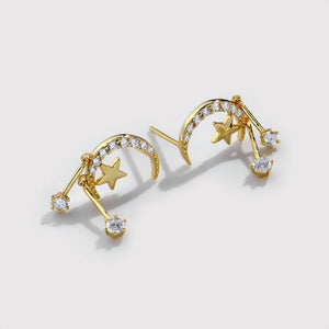Gold earrings with star and moon designs on a light gray background