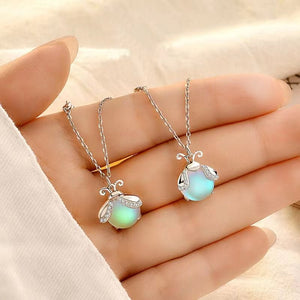 Two silver necklaces with glowing pendants on a hand against a beige background