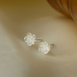 Rose-shaped silver earrings on a beige fabric background
