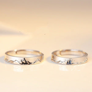 Two silver rings with mountain and wave designs on a beige background