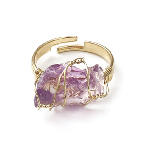 A collection of gold-plated cocktail rings with various colored raw crystal stones, displayed on a white surface.