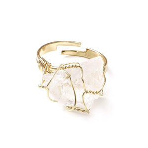 A collection of gold-plated cocktail rings with various colored raw crystal stones, displayed on a white surface.