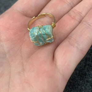 A collection of gold-plated cocktail rings with various colored raw crystal stones, displayed on a white surface.