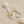 A gold and silver stacking rings with curved wave design, displayed on a beige background with seashells.