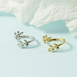 Gold and silver leaf-shaped rings on a light blue background with white fabric.