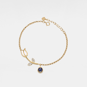 Gold bracelet with leaf and gemstone charm on a light gray background