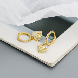A pair of dangle drop hoop earrings with heart and star shapes, featuring gold plating and cubic zirconia embellishments on a white textured surface.