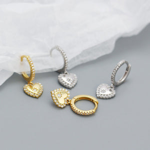 Set of gold and silver heart-shaped earrings on a gray surface with white fabric background