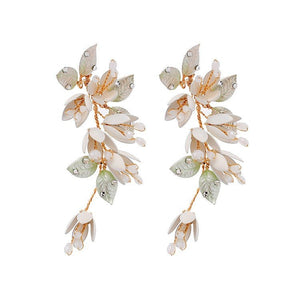 A woman wearing a white dress featuring long dangle drop earrings with gold plating, pearls, and leaf designs.