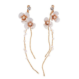 A woman wearing a white dress featuring long dangle drop earrings with gold plating, pearls, and leaf designs.
