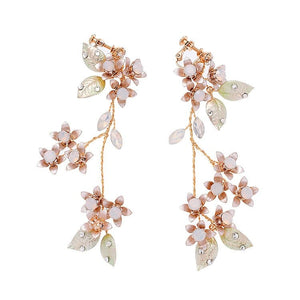 A woman wearing a white dress featuring long dangle drop earrings with gold plating, pearls, and leaf designs.
