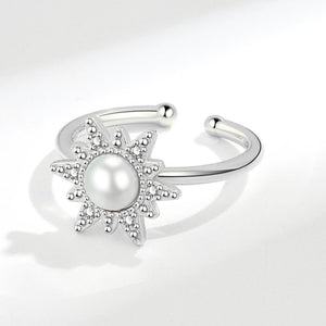 An adjustable spinner ring with a sun motif, featuring a pearl at the center, surrounded by small cubic zirconia stones, with gold plating.