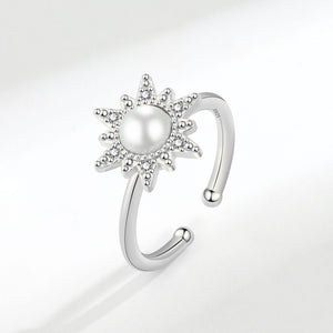 An adjustable spinner ring with a sun motif, featuring a pearl at the center, surrounded by small cubic zirconia stones, with gold plating.