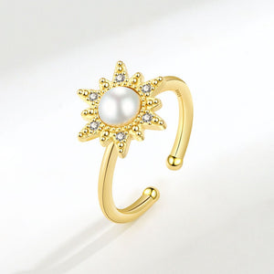 An adjustable spinner ring with a sun motif, featuring a pearl at the center, surrounded by small cubic zirconia stones, with gold plating.