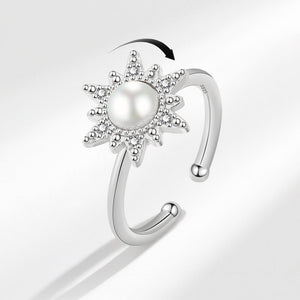 An adjustable spinner ring with a sun motif, featuring a pearl at the center, surrounded by small cubic zirconia stones, with gold plating.