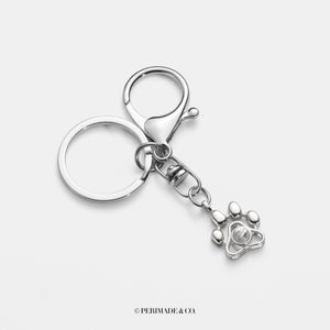 A sterling silver keychain with gold plating, featuring a paw-shaped charm and a small camera.