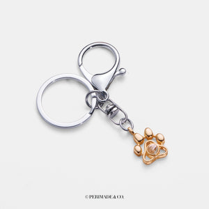 A sterling silver keychain with gold plating, featuring a paw-shaped charm and a small camera.