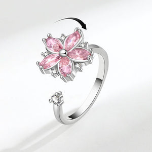 A silver-colored fidget spinner ring with a pink flower design and clear accents, displayed against a white background.