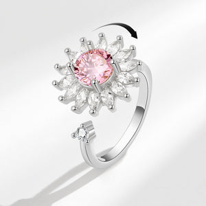 A silver-colored fidget spinner ring with a sunflower design, featuring a pink central stone and clear surrounding stones.