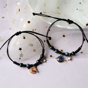 Two black beaded bracelets with star and planet charms on a white background with gold stars.