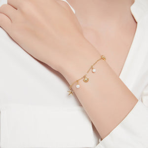 Model wearing a gold bracelet with seashell, starfish and pearl charms